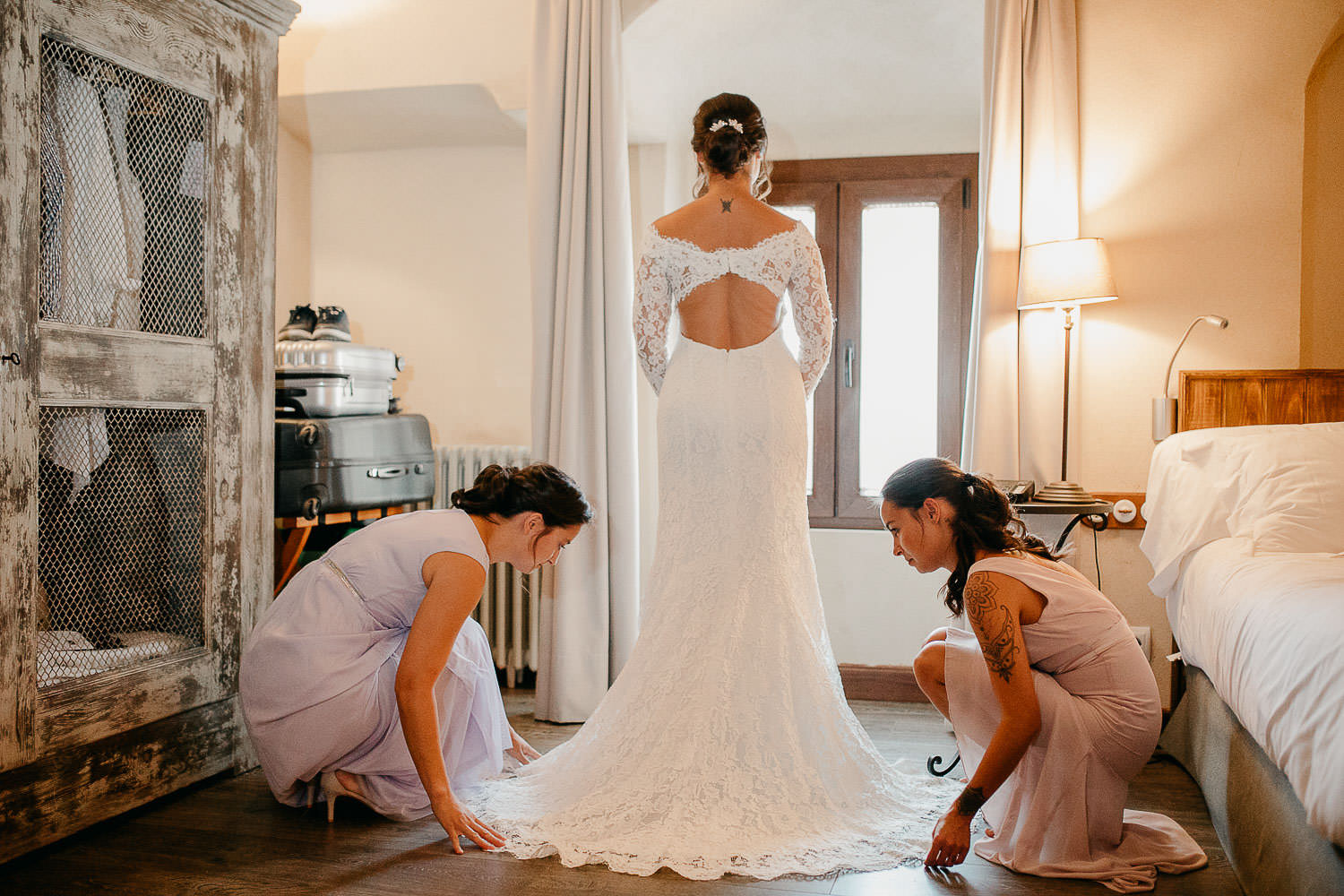 Hermana ayuda a la novia a vestirse, colocando la cola del vestido