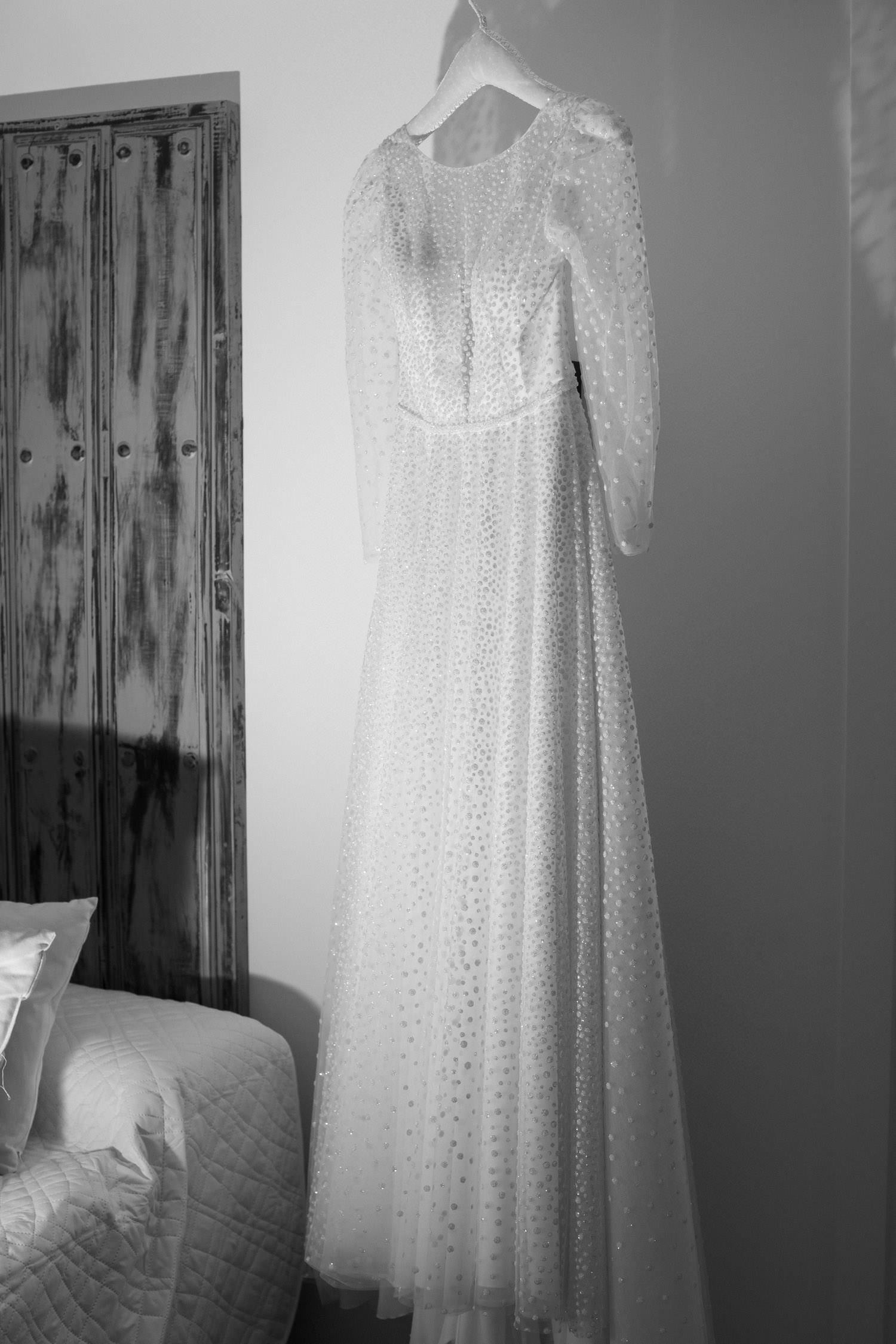 boda de otoño en el Castillo de la Arguijuela 3 Vestido de novia completo colgado en la habitación del alojamiento rural, iluminado por luz suave.