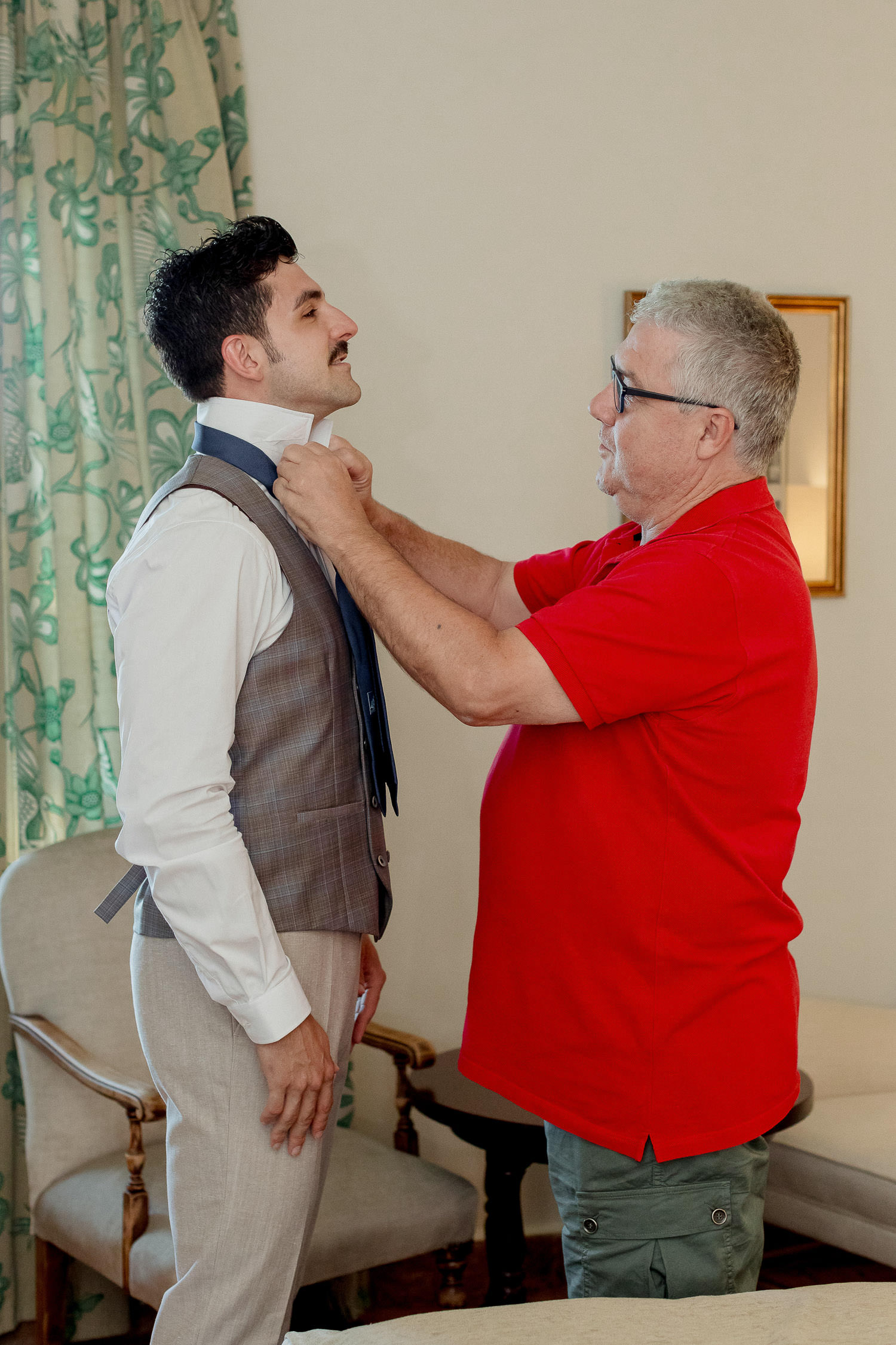 Una boda civil en el Parador de Jarandilla 2 El novio recibe la ayuda de su padre, vestido con camiseta roja, que le ajusta la corbata en un ambiente cálido y familiar, representando el apoyo y la complicidad antes de la ceremonia.