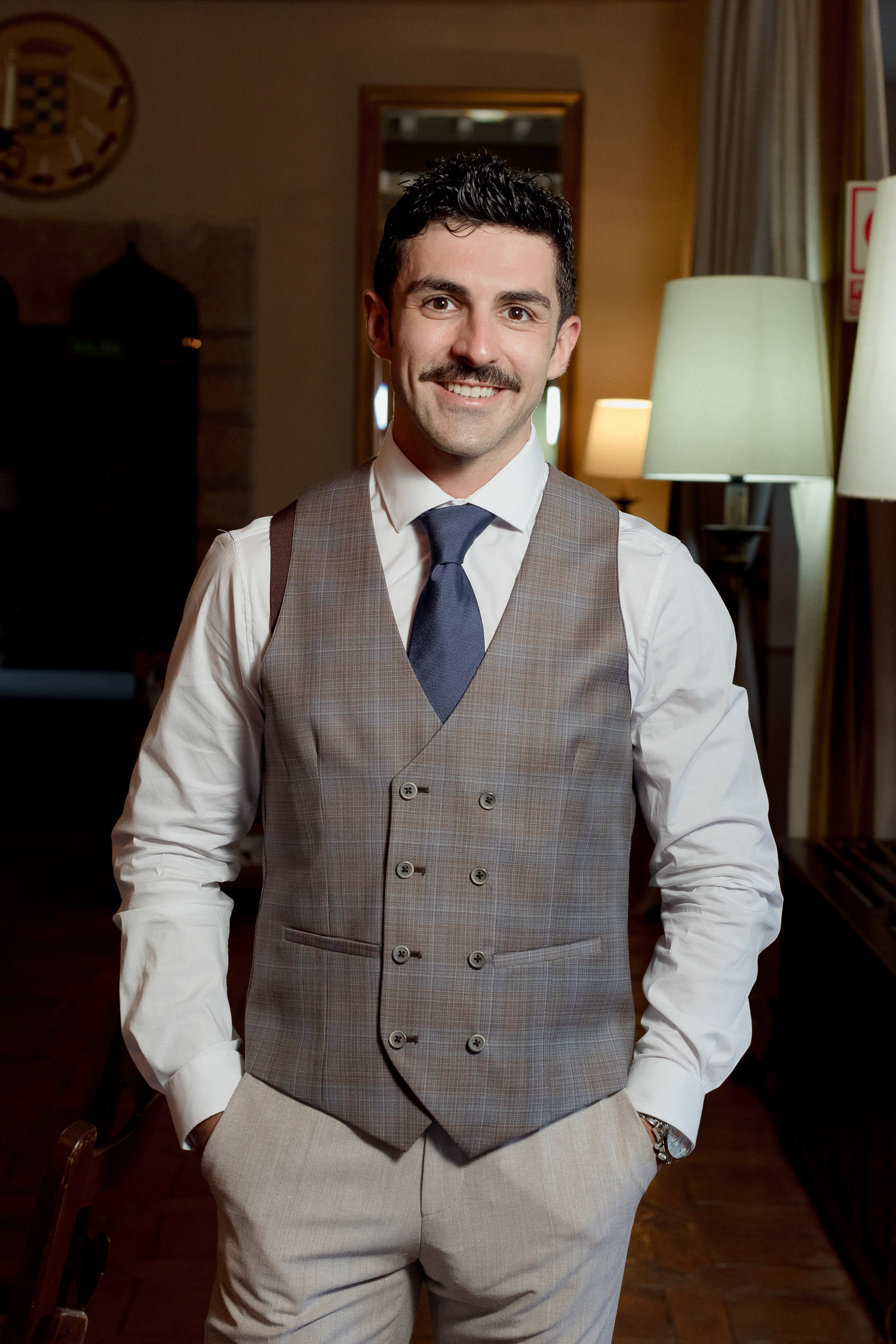 Una boda civil en el Parador de Jarandilla 5 Un primer plano del novio, con expresión relajada y una ligera sonrisa, luce su chaleco y camisa blanca mientras se prepara para su gran día, rodeado de un ambiente elegante y luminoso.