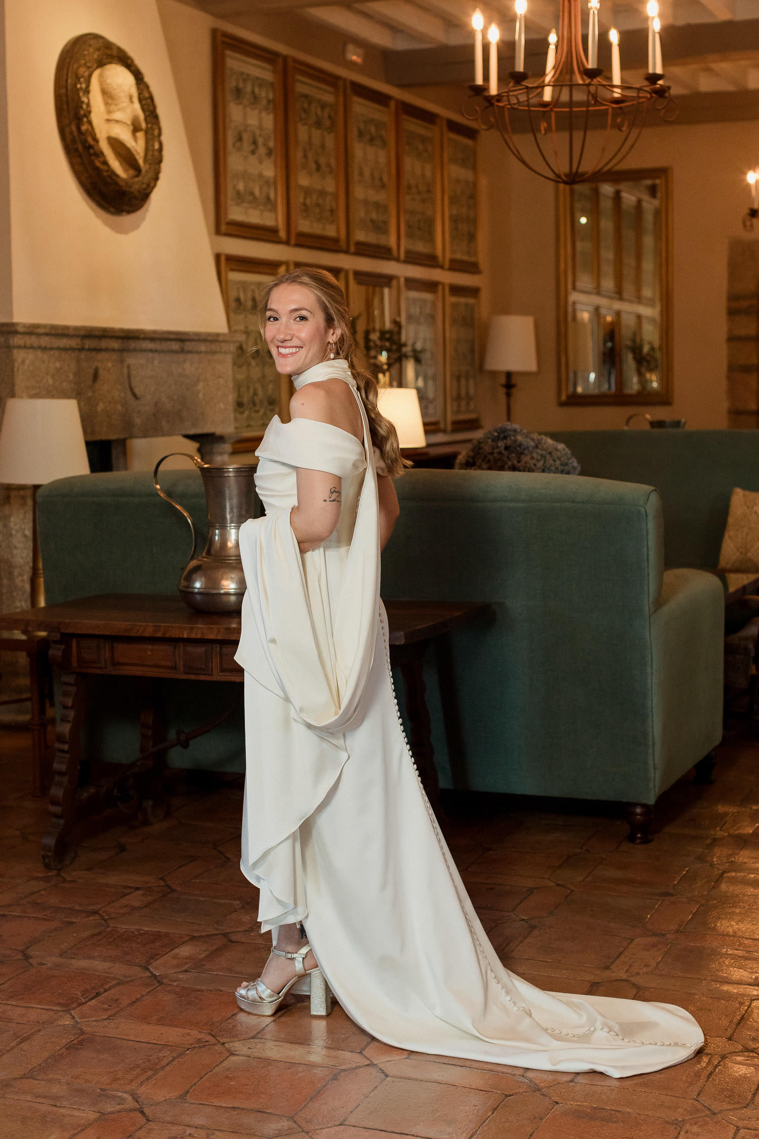 Una boda civil en el Parador de Jarandilla 19 La novia posa con confianza en el salón de un elegante parador, luciendo un vestido blanco con escote barco y una larga cola, con una gran sonrisa y un aire relajado.